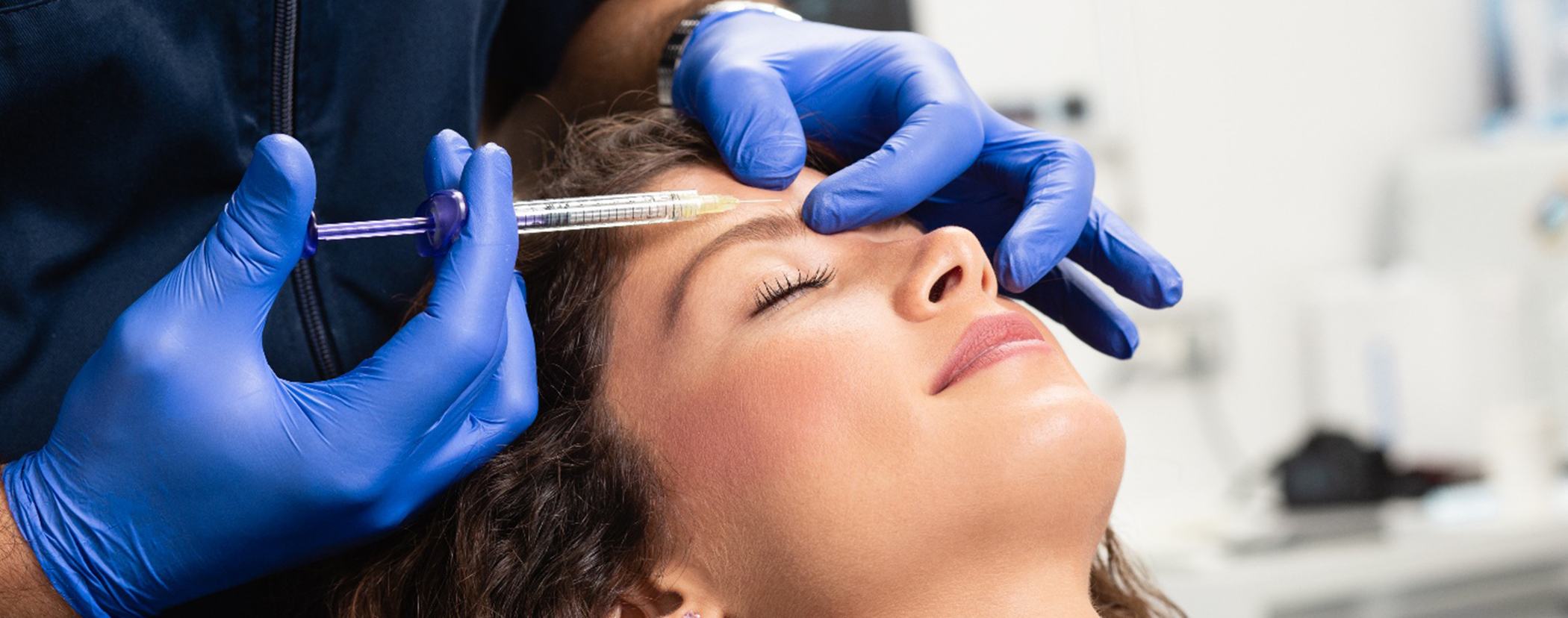 Blue-gloved hands applying injection to woman’s forehead