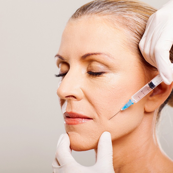 Gloved hands applying injectable to older woman’s cheek/jaw