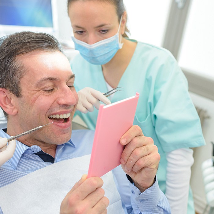 Someone in blue gloves holding sample dental crown to model abutment tooth