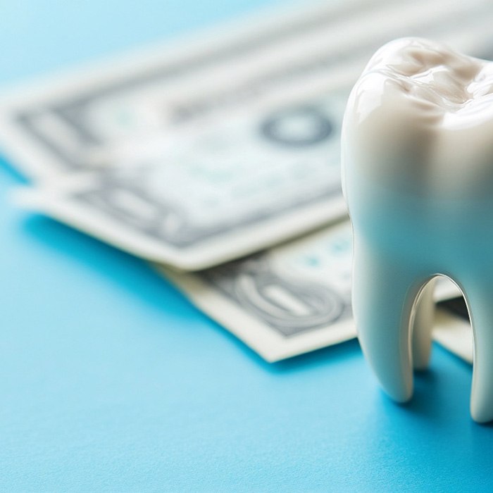 Large model tooth next to dollar bills on blue surface