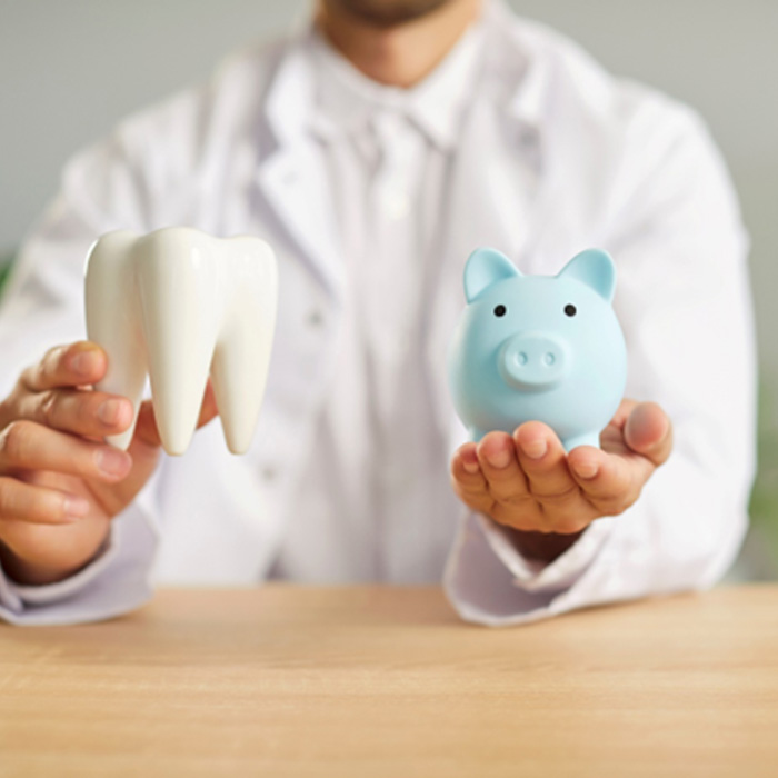 Dentist in white coat holding model tooth and blue piggy bank